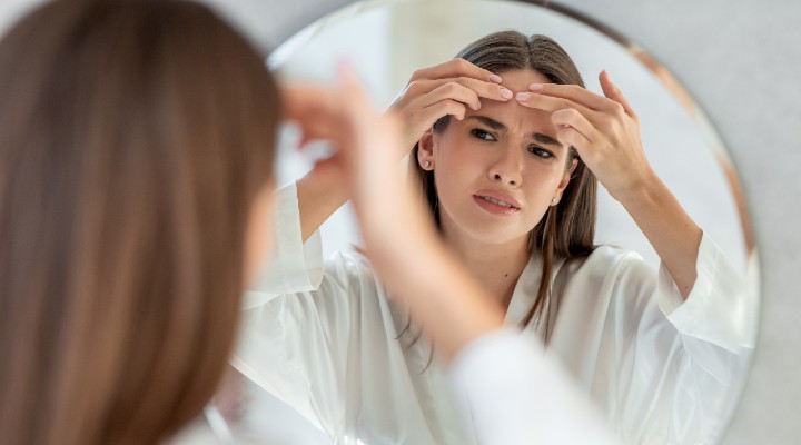 Woman tries to pop a pimple while looking in the mirror.